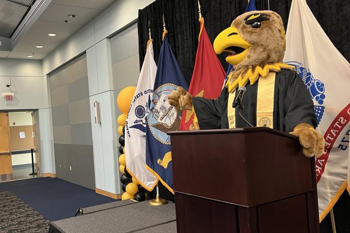 金鹰埃迪穿着毕业礼服，站在讲台上.